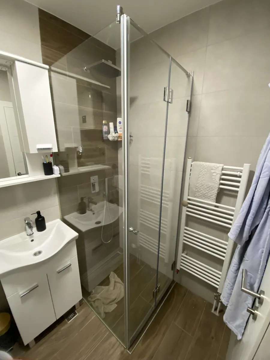 Zatvorena preklopna tuš kabina na L: fiksno staklo uz lavabo i preklopna vrata od dva krila sa sjajnim šarkama